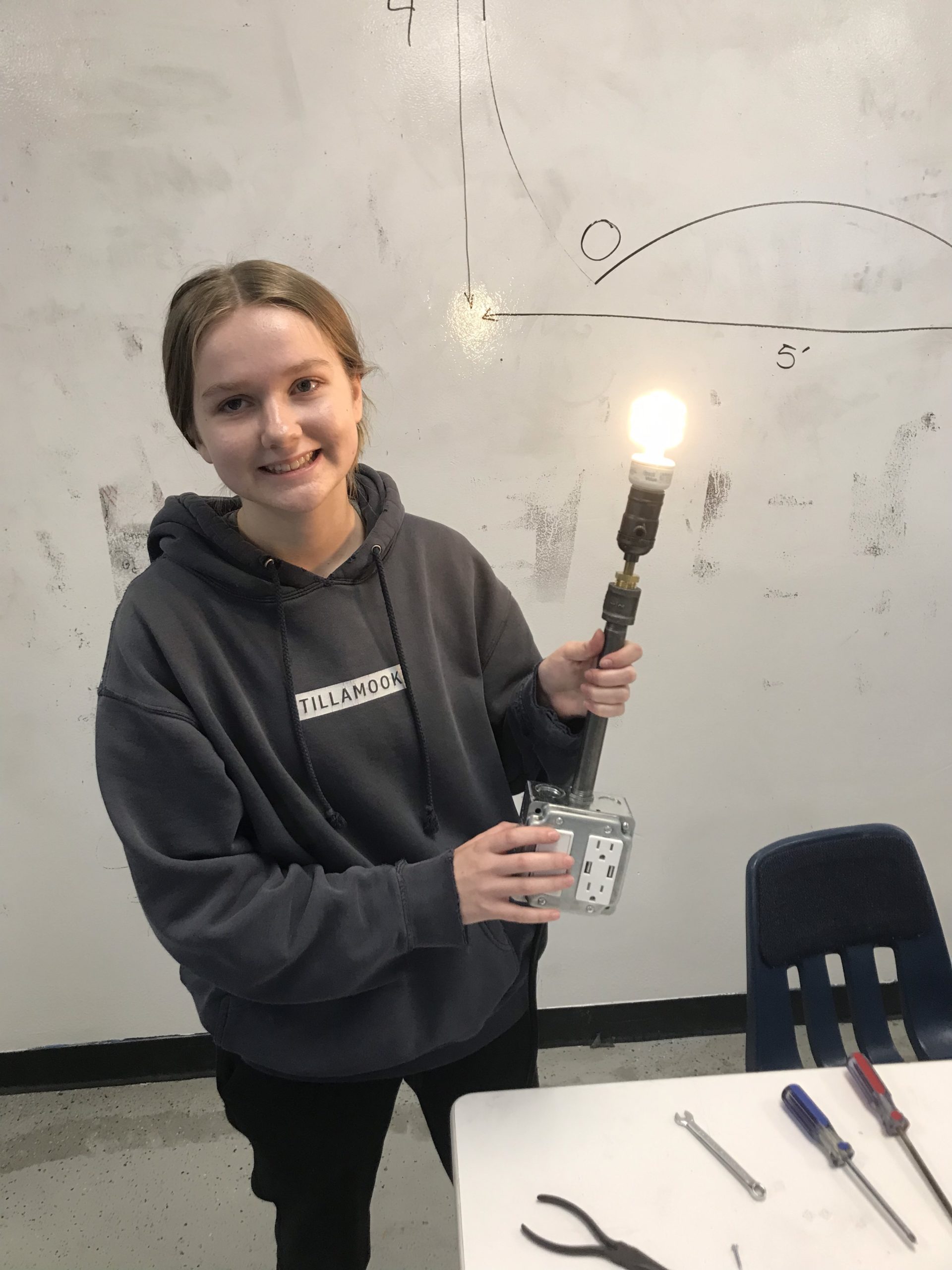 A smiling SET High student holds a bright lightbulb attached to their electric switch they created in engineering class. STEM rules!