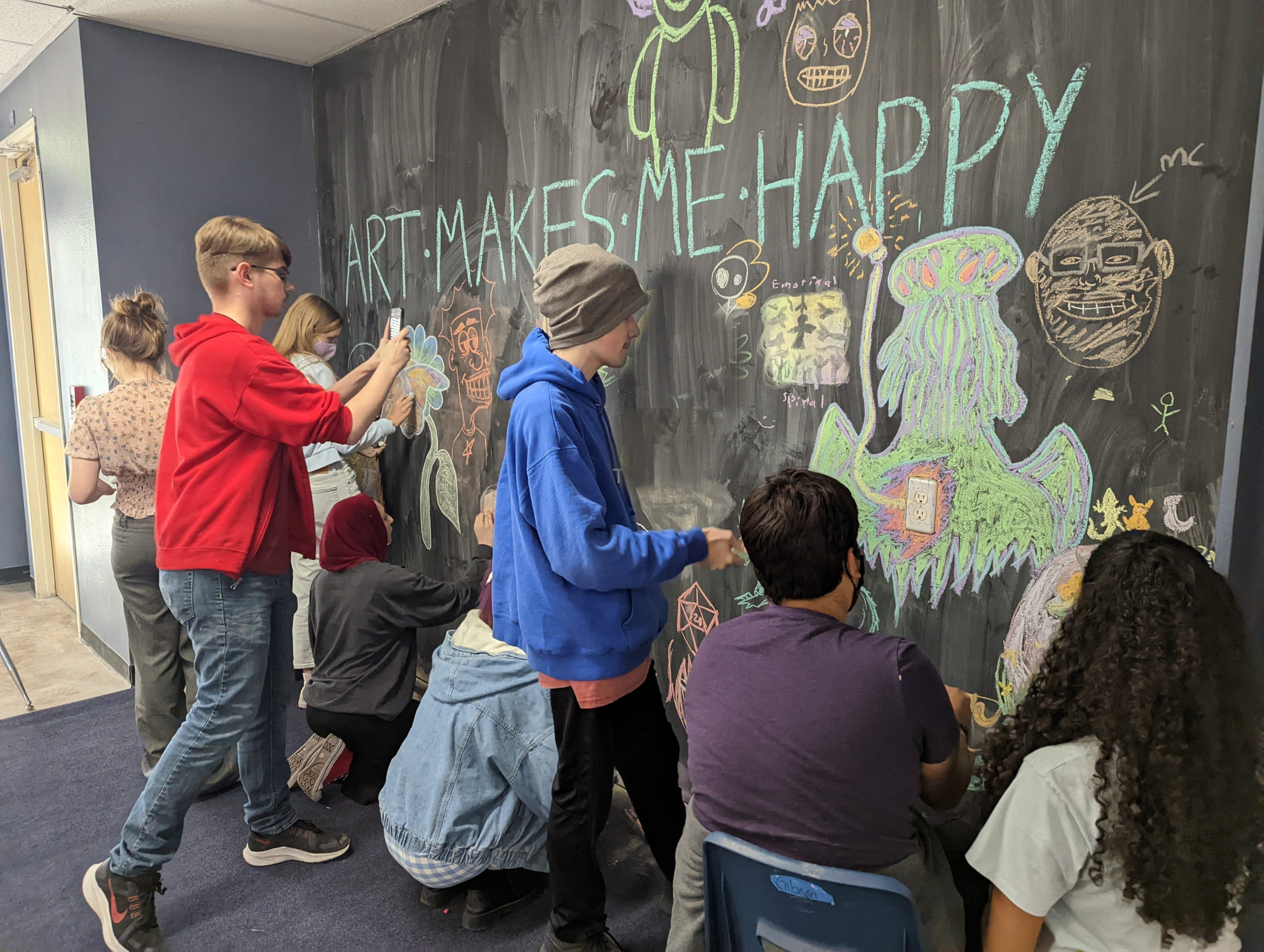 SET High students create a collaborative work of art with the message, "ART MAKES ME HAPPY" on the Chalk Space wall.