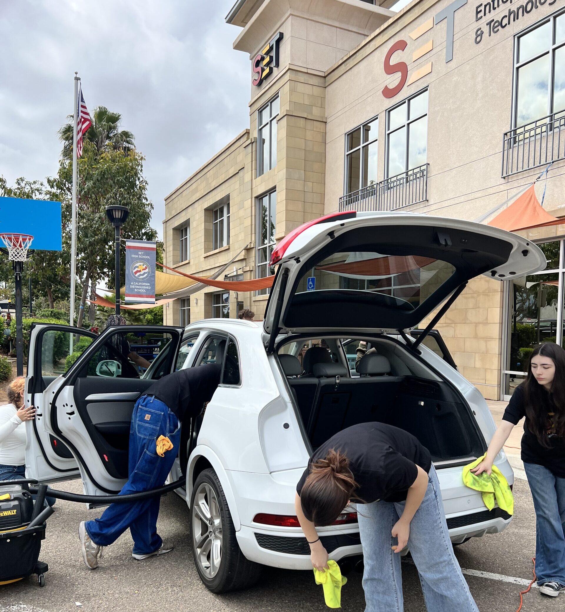 The School for Entrepreneurship & Technology students vacuum and wipe down a white car outside the school’s two story building