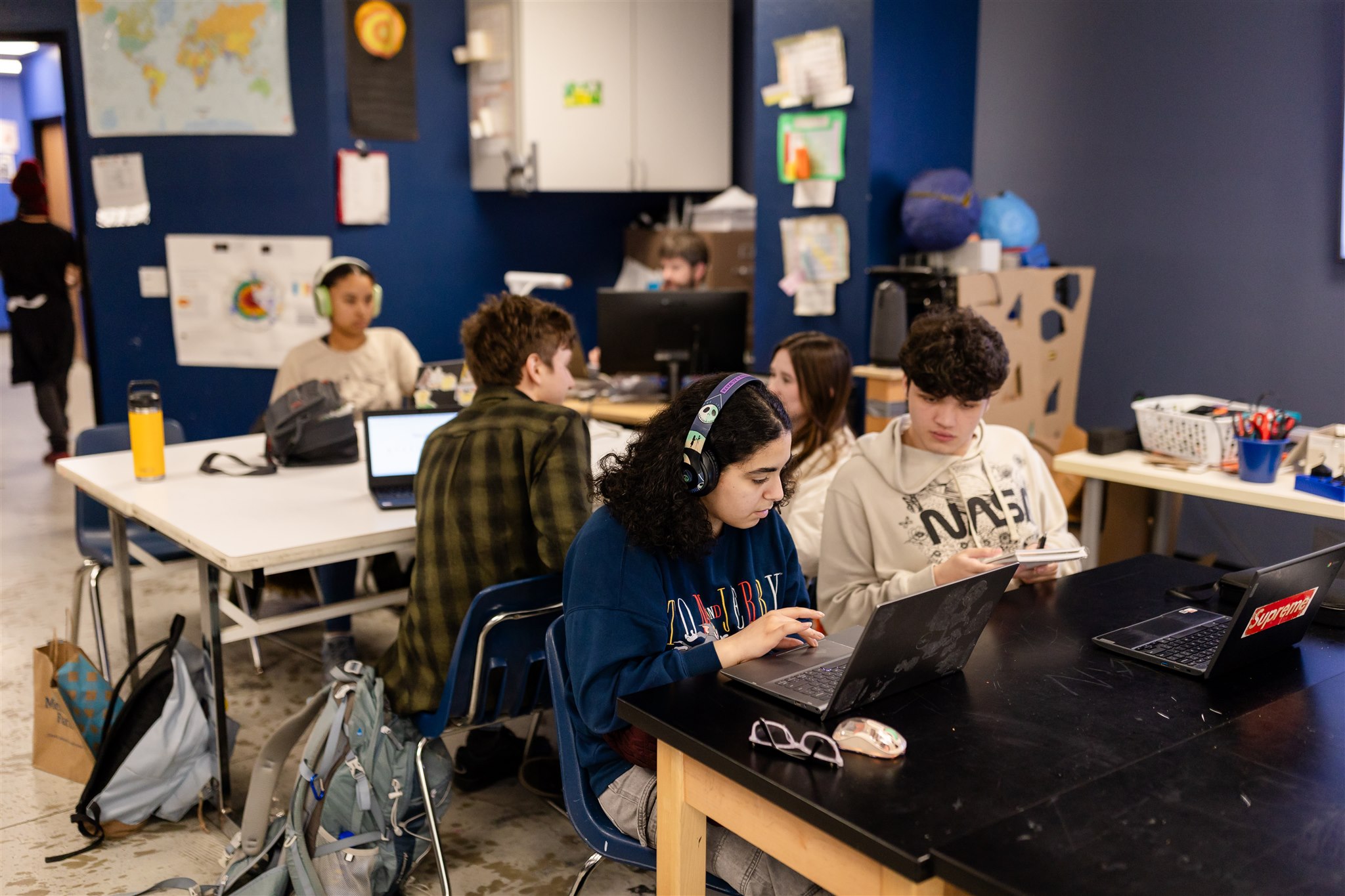 SET High students sit at a couple of large tables in a classroom working and talking in pairs on laptops.
