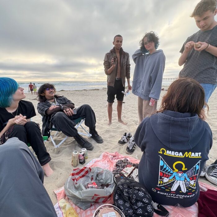 A group of young people (including SET High graduate Nadia Reyes) sit on a sandy beach with the ocean and cloudy sky in the background.