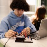 A SET High student sits at a classroom table working on a wiring project with a laptop next to them.