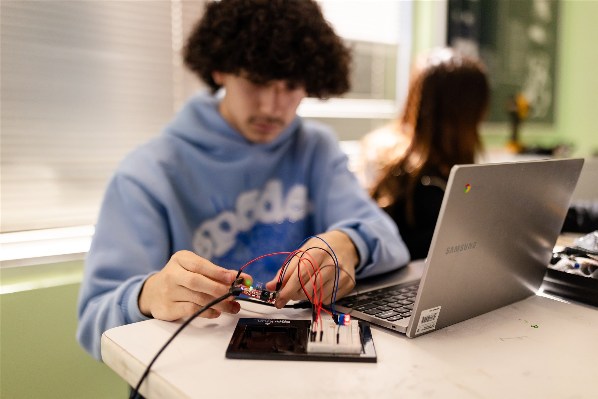 A SET High student sits at a classroom table working on a wiring project with a laptop next to them.