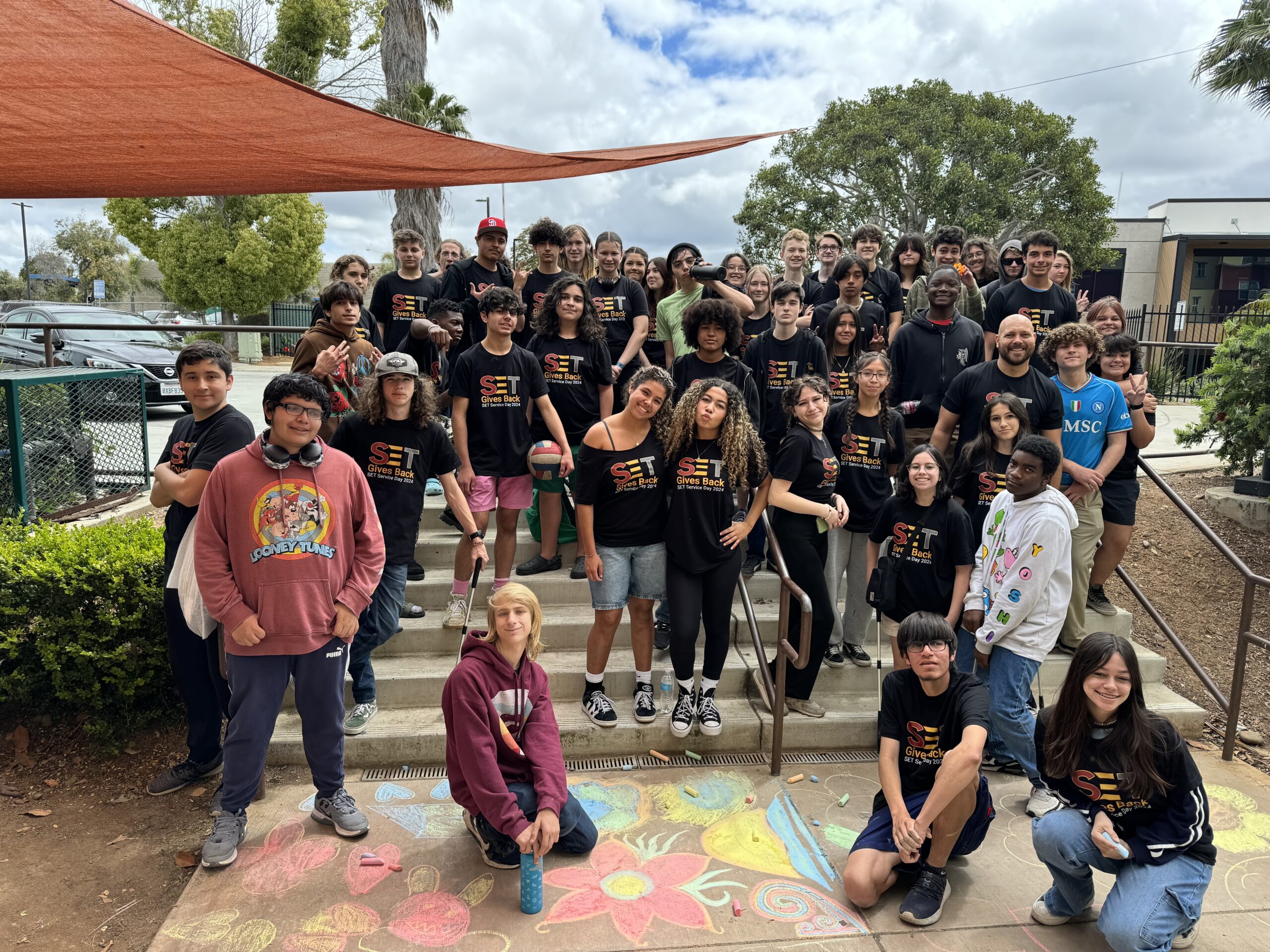A group of SET High students, mostly in black t-shirts with “SET” written on them, stand on concrete steps outside the school.